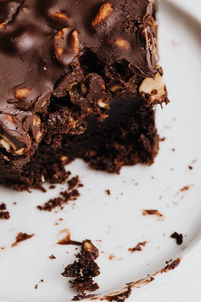 Close-up of a decadent chocolate brownie with nuts on a white plate.
